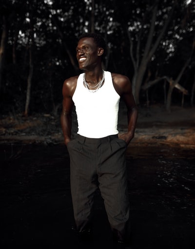 man in white tank top and gray pants standing on dirt road